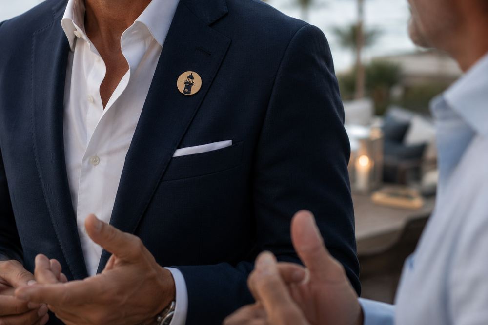 Primer plano de un pequeño pin dorado con un faro en la solapa de una americana azul marino, en un encuentro de SAL.